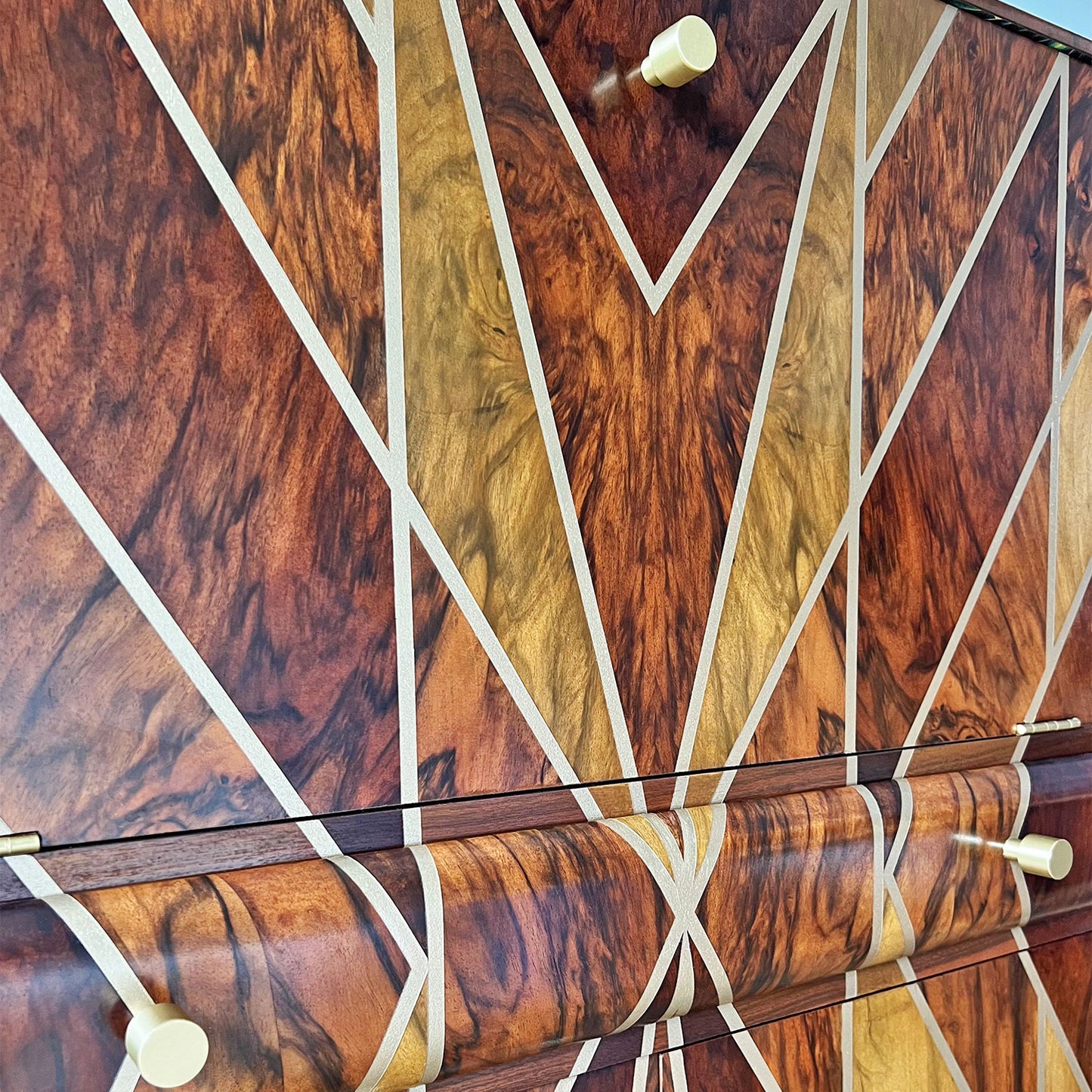 Close-up of solid brass handles – Elegant solid brass hardware, complementing the luxury Art Deco aesthetic of this handcrafted cabinet. Hand-applied metallic gold paint and wood dyes creating a striking Art Deco pattern on the walnut grain.